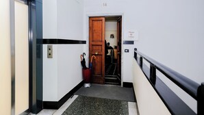 Un pasillo con una puerta de madera con el número 14, un botiquín para paraguas rojo y una pared blanco y negro con una banda negra.