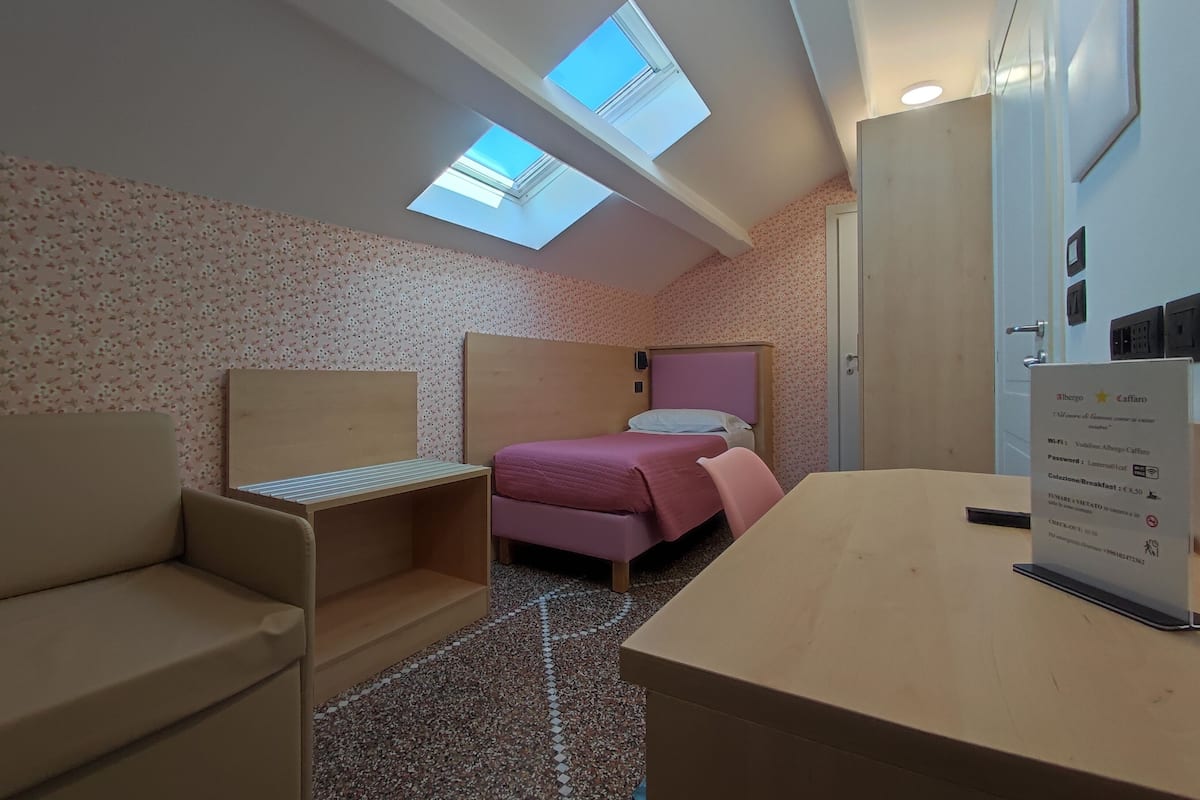 A room with a bed, a desk, a chair, and two skylights.