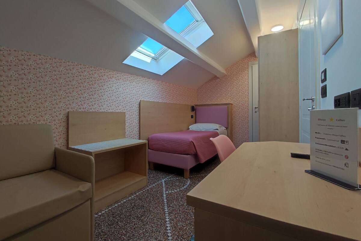 A room with a bed, a desk, a chair, and two skylights.