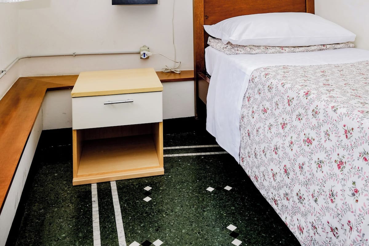 A bedroom with a bunk bed, a bedside table with a lamp, a small drawer, and a bed with a floral bedspread.