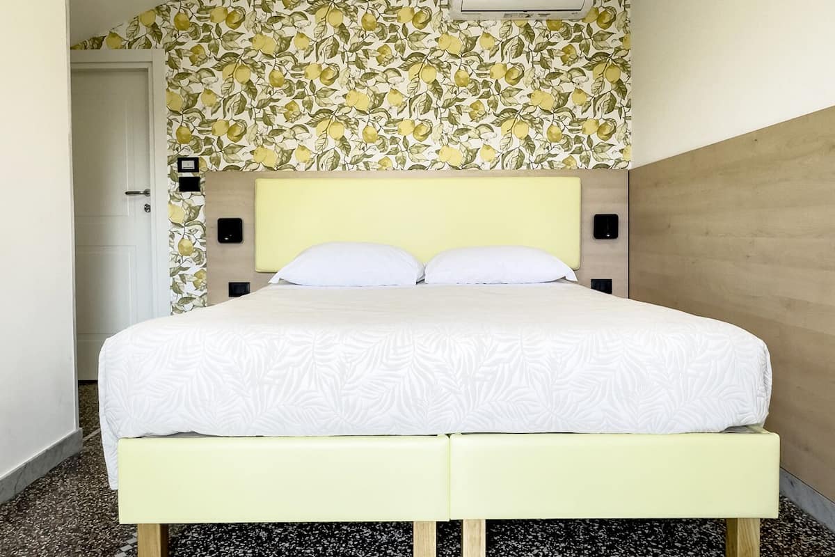 A bed with a white bedspread, two white pillows, a yellow headboard, and a floral wallpaper pattern above.