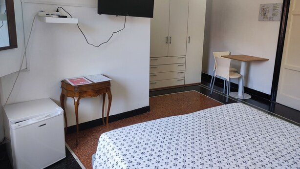 A hotel room with a bed, a small desk, a wardrobe, and a television mounted on the wall. - Albergo Caffaro (Genoa)