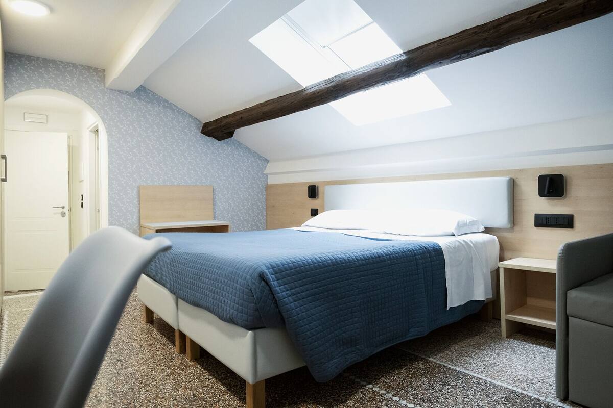 A bedroom with a bed, bedside tables, a chair, a wardrobe, and a skylight.