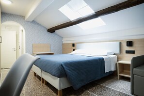 Un dormitorio con cama, mesitas de noche, una silla, armario y tragaluz.