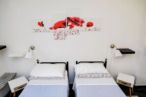 Habitación con dos camas, ropa de cama blanca, una mesita, una silla y lámparas fijadas a la pared.