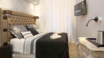 Een net opgemaakt bed met een zwart-wit gebedruid sprei, een gestoffeerd hoofdbord en decoratieve kussens. Een flatscreen televisie aan de muur toont de titel van een film.
