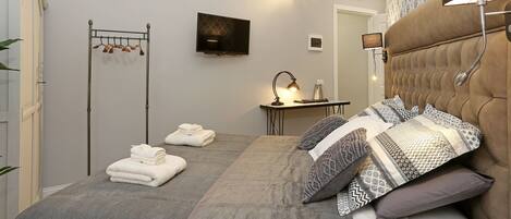 A bedroom with a bed, a TV, a desk, and a mirror.