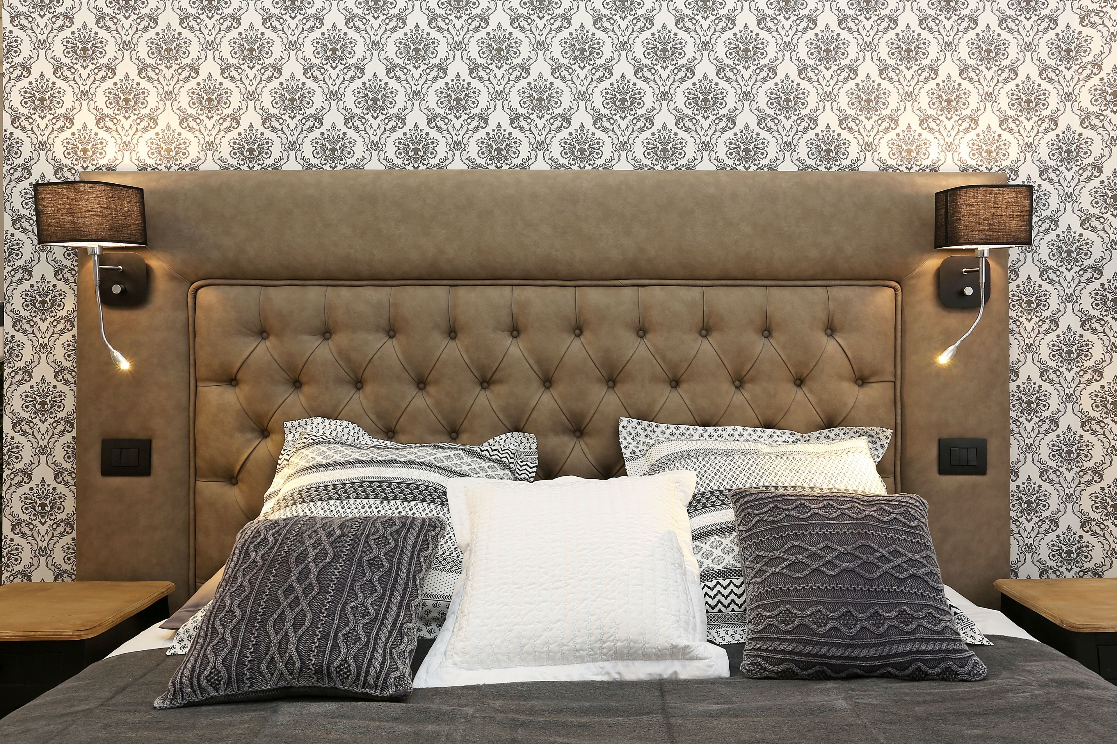 A bedroom with a tufted headboard, patterned bedding, and wall-mounted lamps.