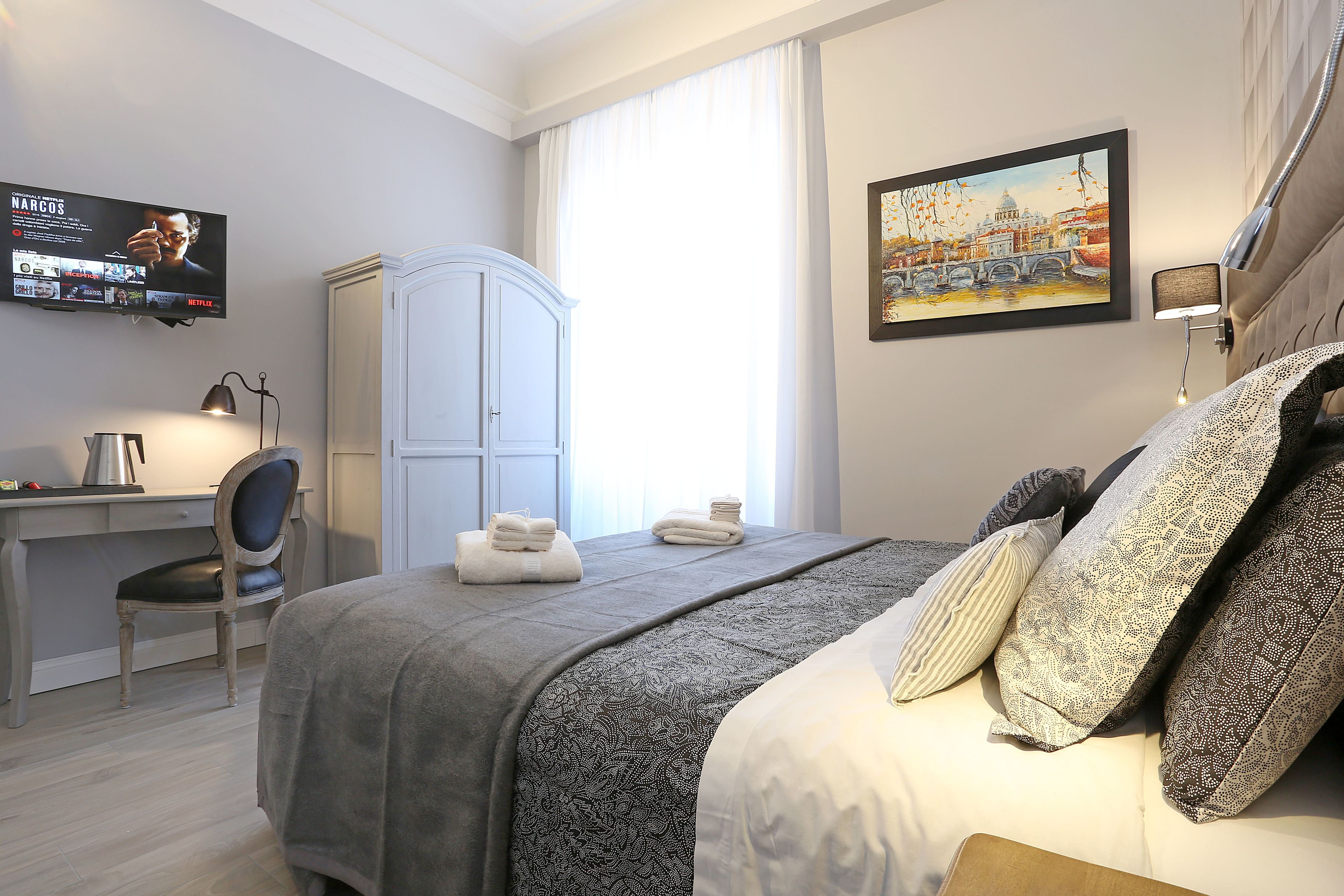 Habitació d'hotel amb un llit, una taula de nit amb cadira, un armari, una televisió i un quadre a la paret.