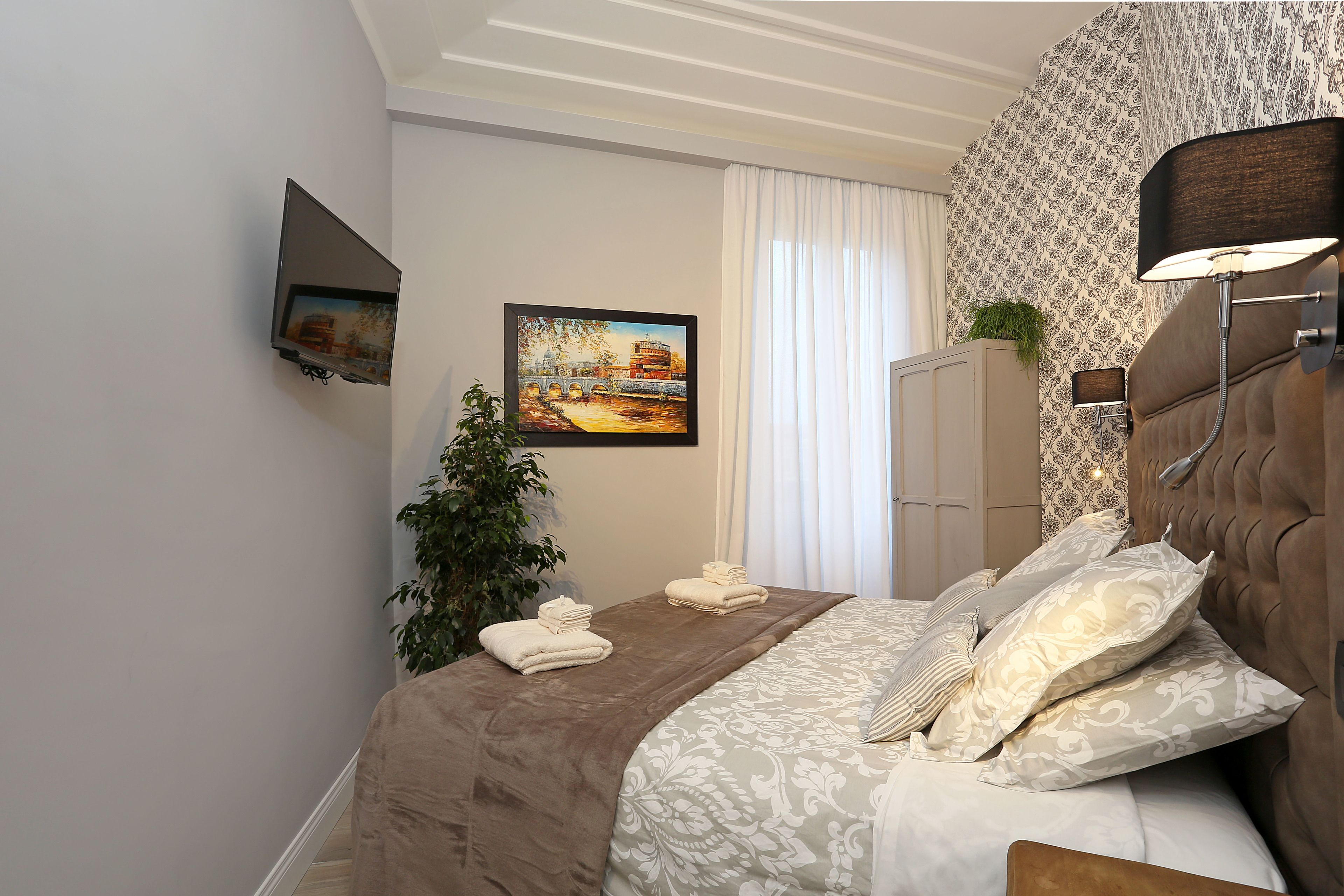 Une chambre à coucher bien rangée, avec un lit, un téléviseur fixé au mur, un tableau et une plante.