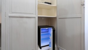 A compact, white-framed walk-in closet with a built-in black refrigerator and a shelf above it. - Capricci Romani (Rome)