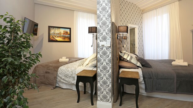 A bedroom with two beds, a large mirror, a potted plant, and a painting on the wall. - Capricci Romani (Rome)