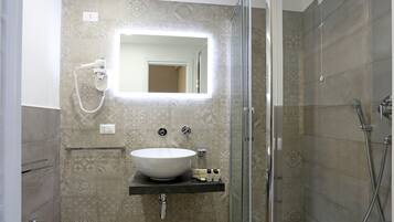 A bathroom with a large mirror, a white sink, a shower, and a toilet.