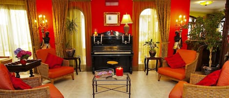 A living room with a piano, wicker chairs, a coffee table, and red walls.