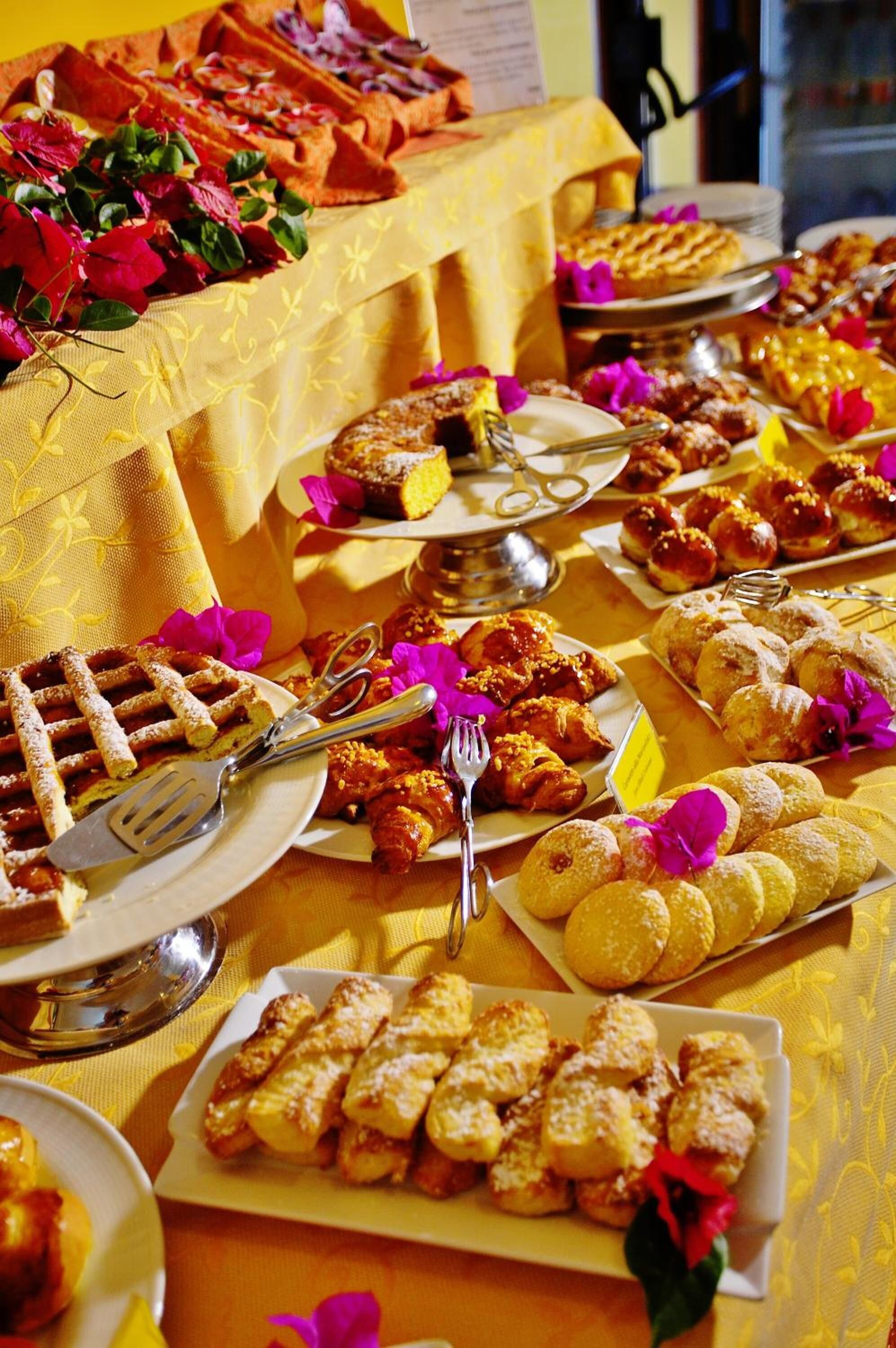 Een buffettafel met diverse gebakjes en desserts, waaronder wafels, croissants en ander vers gebak, gepresenteerd op borden en serveerplanken.