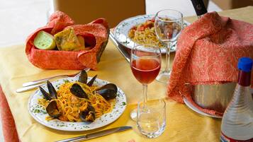 Ein Esstisch mit einer Pasta-Servierplatte, einem Glas Rotwein und einer Wasserflasche.