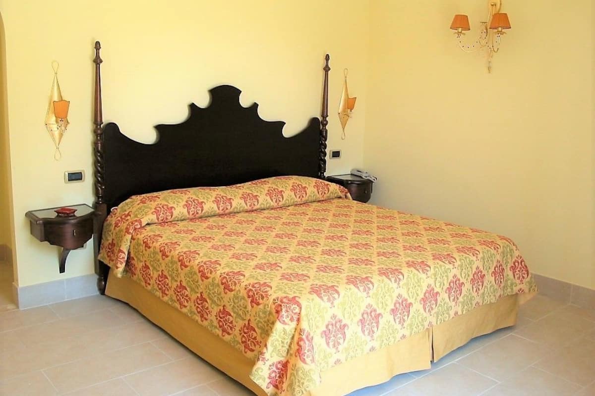 A bedroom with a large bed, two bedside tables, and wall-mounted lamps.
