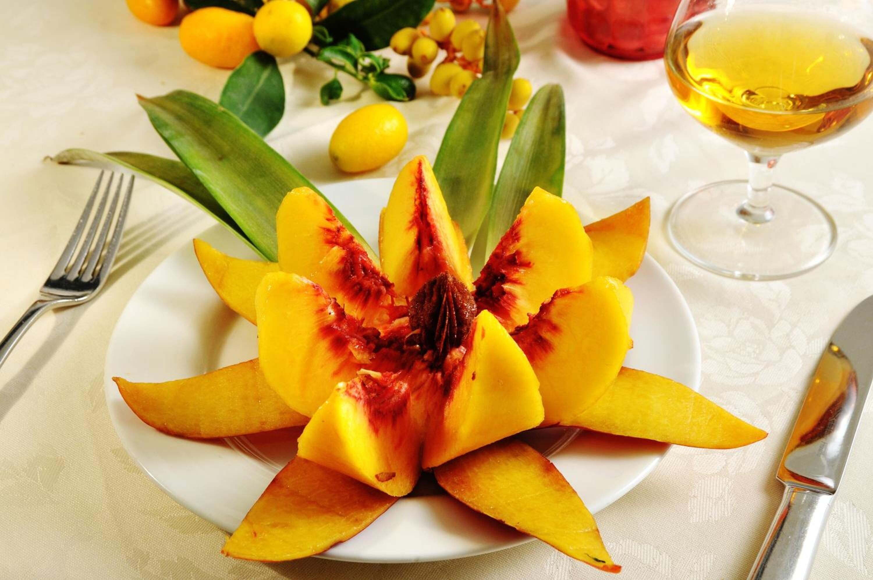 A plate of sliced mango with a glass of juice and a fork on a table.
