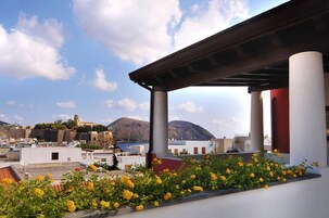 Una terraza en la azotea con flores amarillas, columnas blancas y vistas a un edificio histórico y montañas.