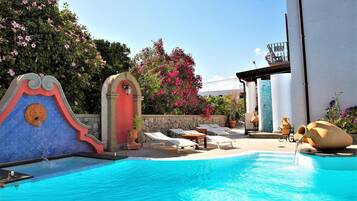 Una piscina con sillas de descanso y una fuente decorativa.