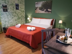 Ett hotellrum med en säng, två sänglampor, ett nattduksbord i trä, ett matbord med en flaska och ett glas samt en stol.