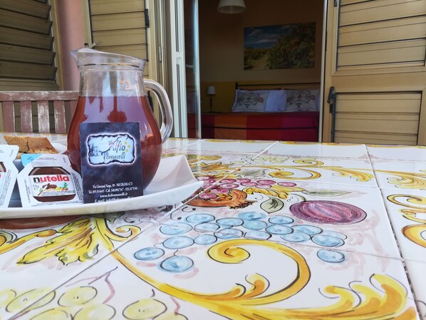 Una mesa con un mantel colorido, una jarra de vidrio y un plato con Nutella y una tarjeta de presentación.