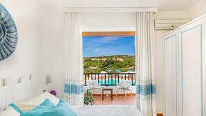 Un dormitorio con balcón, cama, mesa y vistas a una piscina y paisaje.