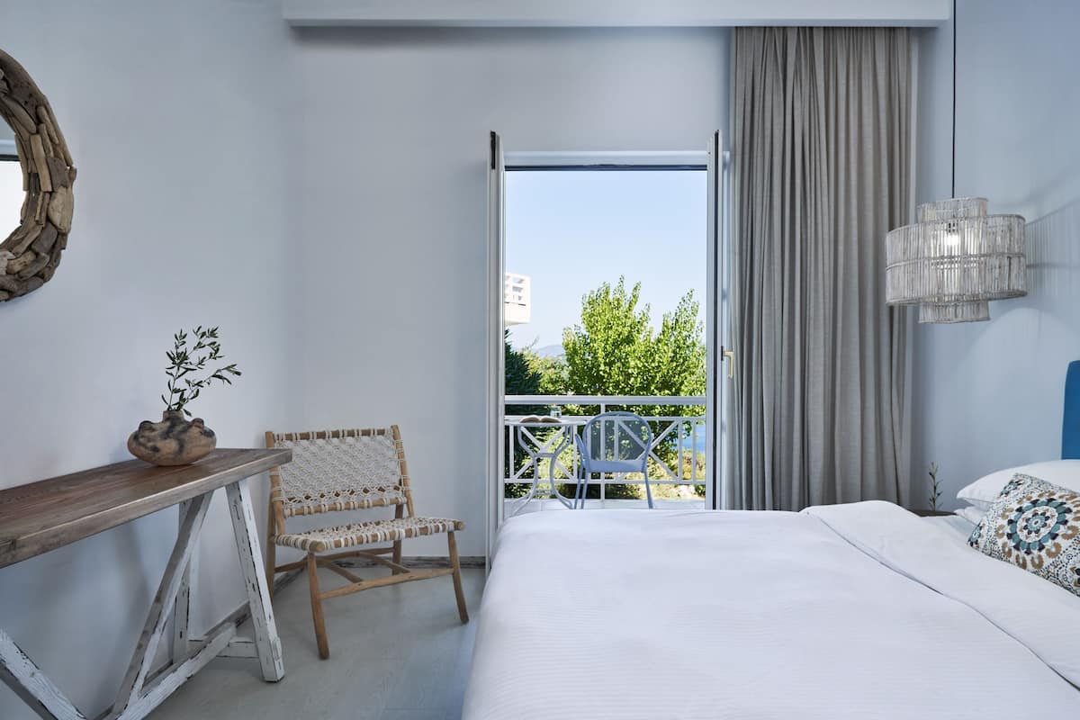 A modern bedroom with a bed, a wooden desk, a wicker chair, a balcony with a railing, and a large mirror on the wall.