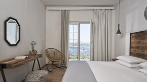 Une chambre avec un grand lit, un bureau en bois, une chaise et une vue sur un balcon équipé d’une table et de chaises.