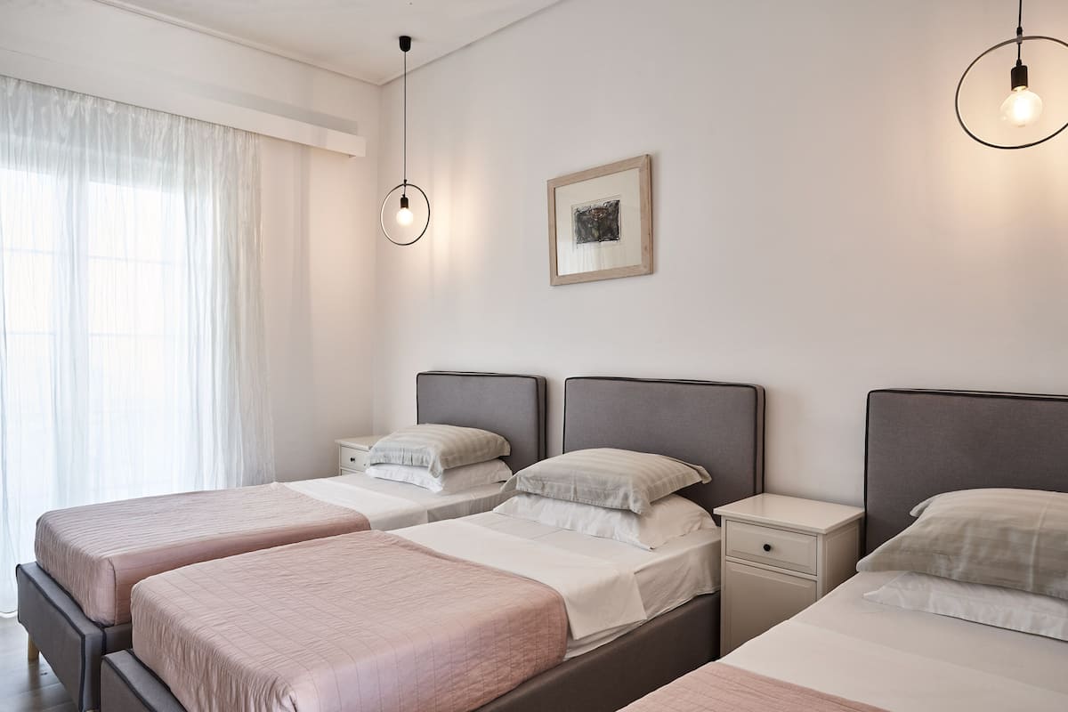 A hotel room with three beds, a bedside table, a nightstand, a framed picture on the wall, and a hanging light fixture.