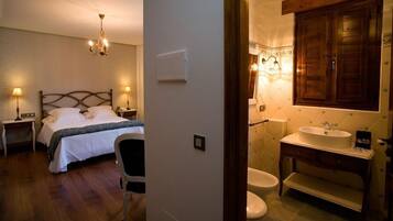 Un dormitorio con cama, lámparas de noche, una silla y un baño con lavamanos, inodoro y armarios de madera.