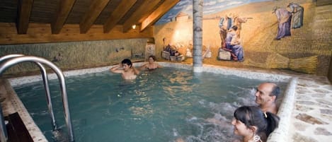 A hot spring area with wooden beams, stone walls, and a mural depicting historical figures.