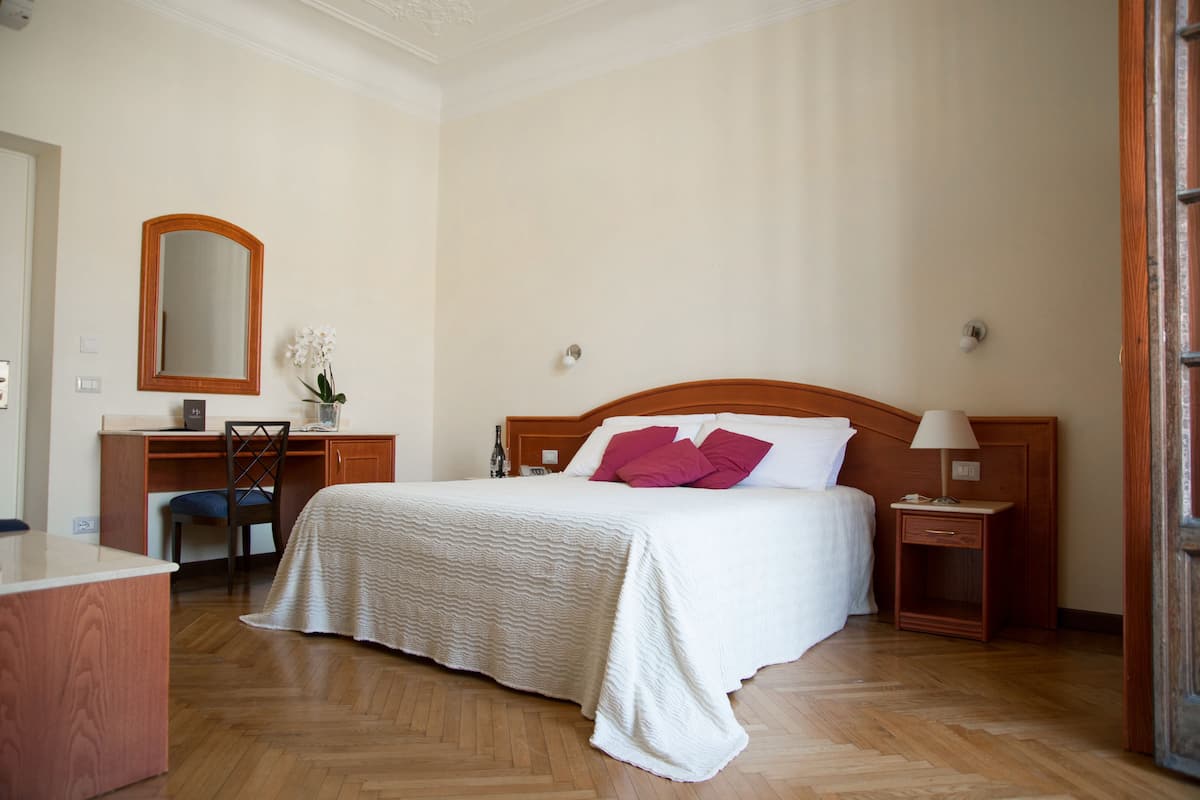 Ein ordentlich eingerichtetes Hotelzimmer mit Bett, Schreibtisch, Stuhl, Nachttisch und Spiegel.