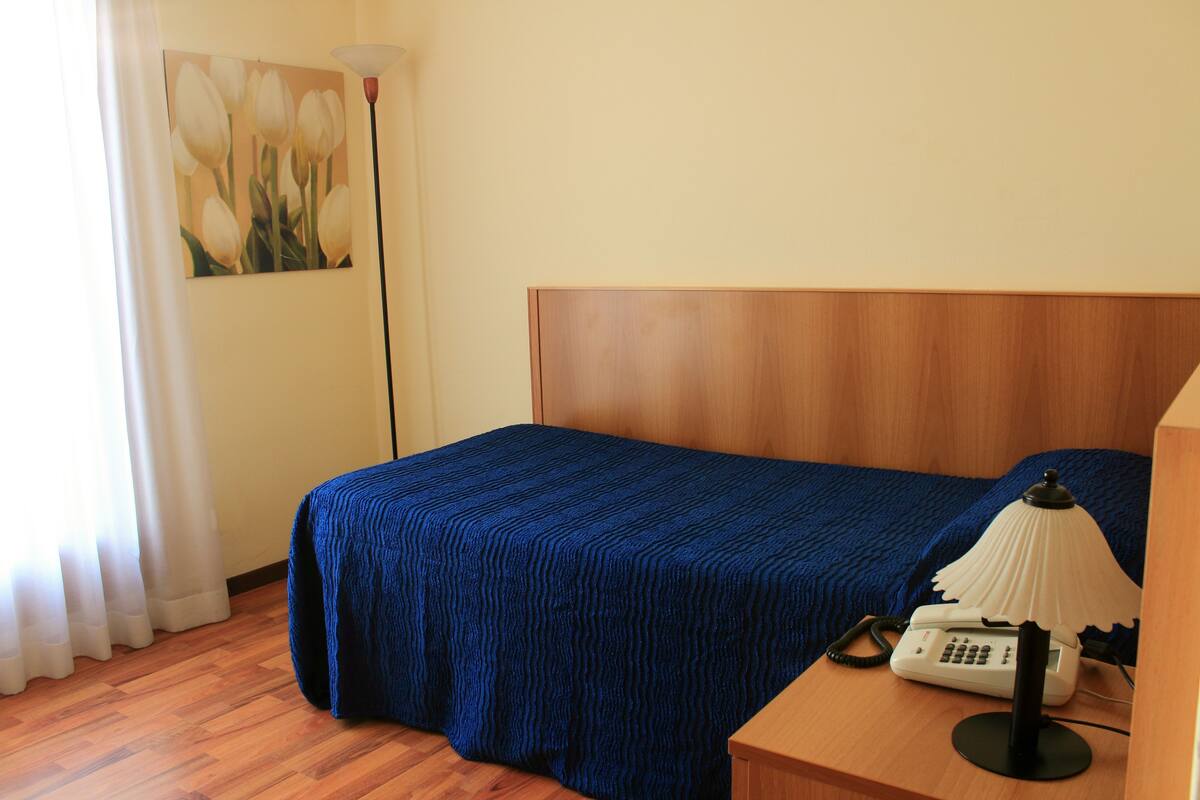 Ein Hotelzimmer mit einem hölzernen Kopfende, einer blauen Bettdecke, einer Nachttischlampe und einem Telefon auf dem Nachttisch.