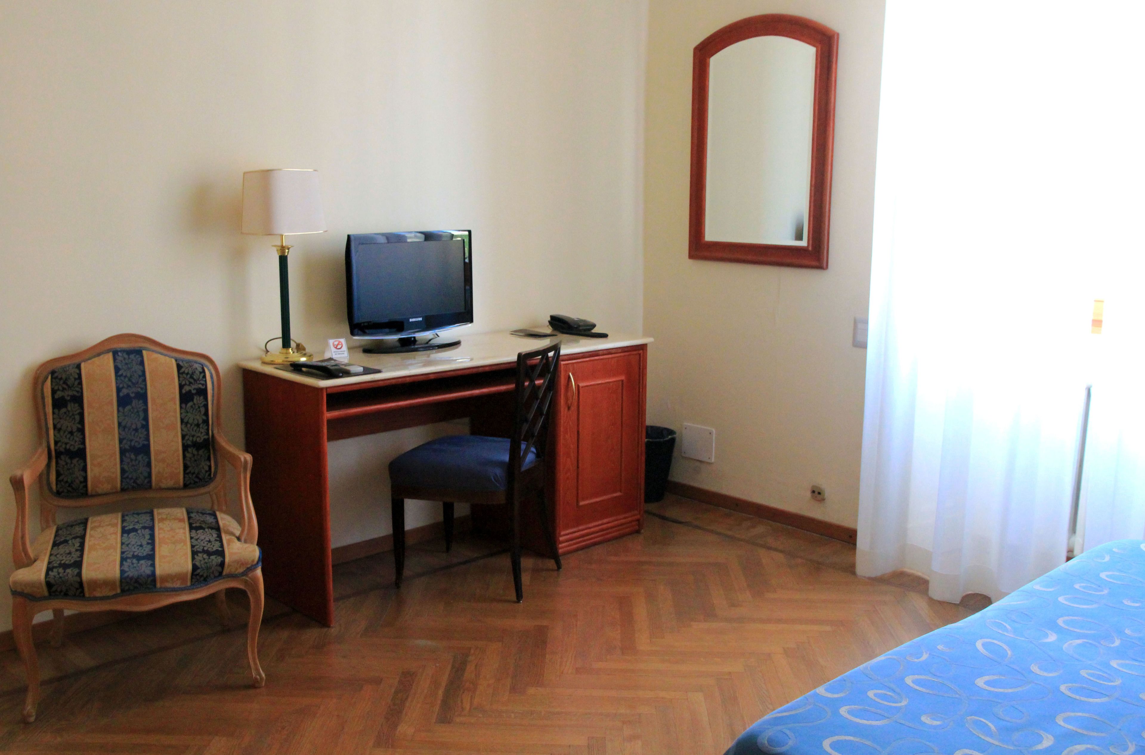 Une chambre d’hôtel avec un bureau en bois, une télévision, une chaise, un lit et un miroir.
