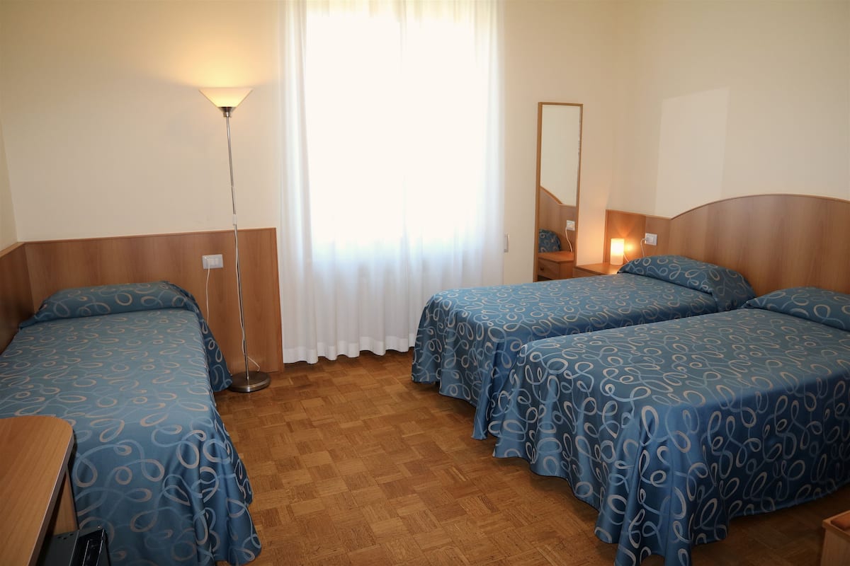 Ein Hotelzimmer mit zwei Betten, einem Schreibtisch, einem Spiegel und einer Stehlampe.