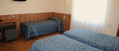 A hotel room with two beds, a desk, a small fridge, and a TV on the wall.