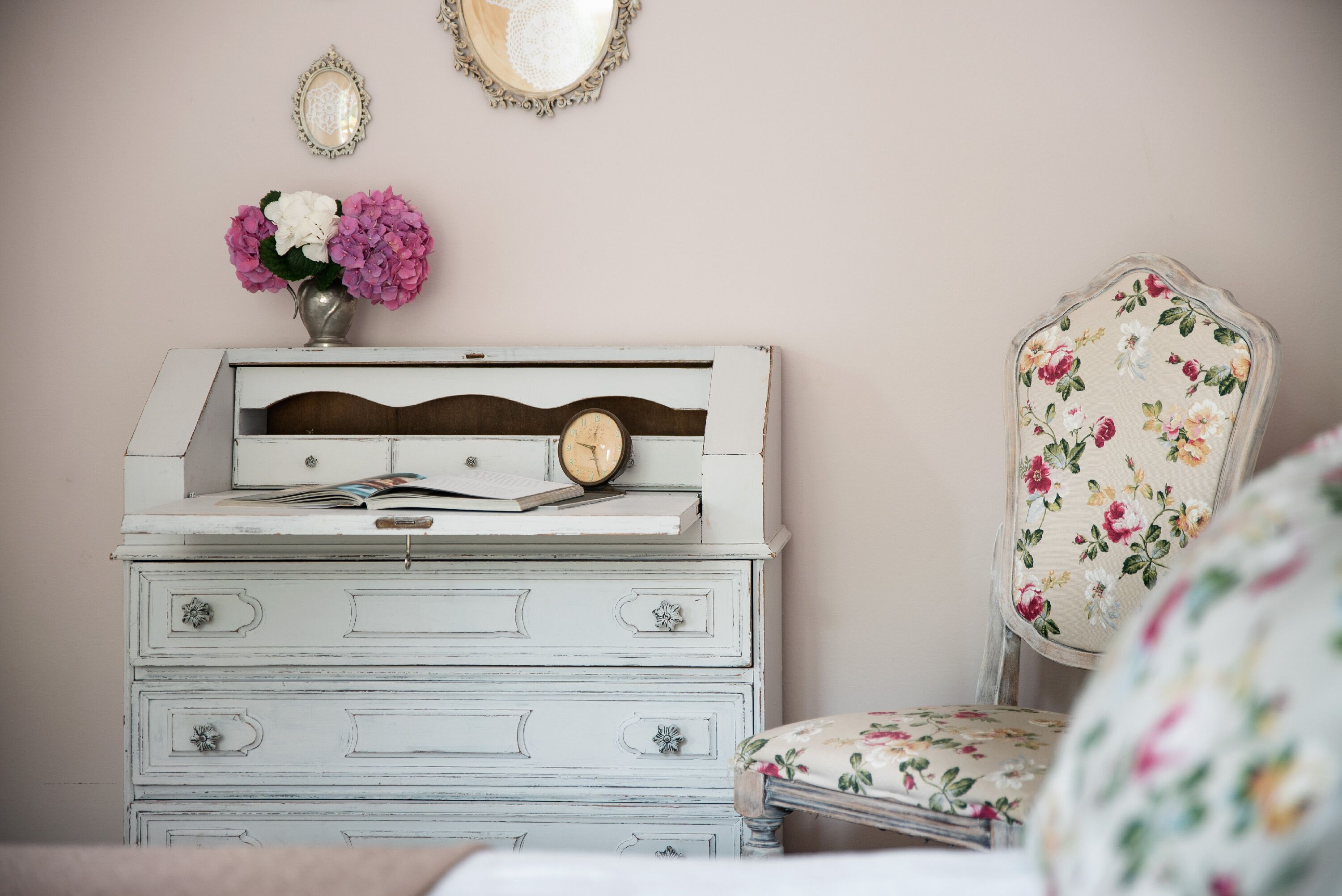 Une commode de style ancien, dotée de tiroirs, sur laquelle sont posés une horloge et un vase de fleurs.