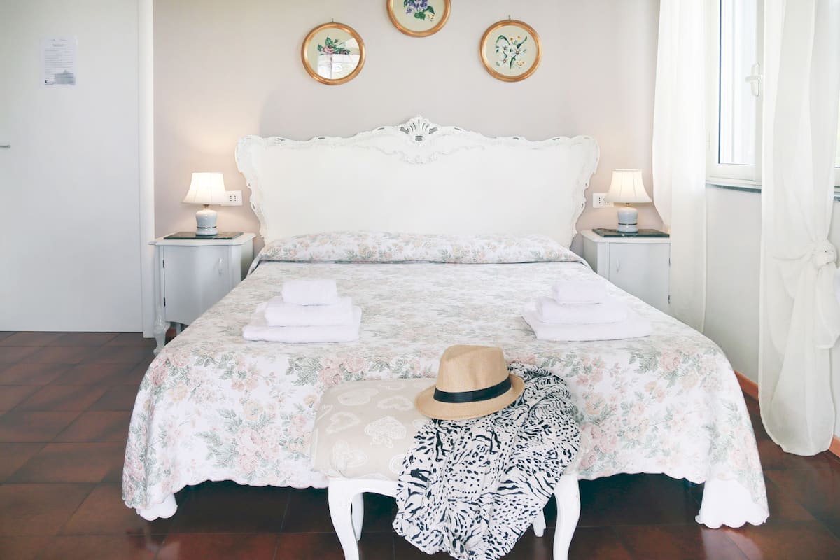 Ein ordentlich bezogenes Bett mit Blumenmuster, zwei Nachttischlampen und ein Hut auf dem Bett.