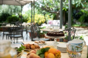 Un área de comedor al aire libre con mesas, sillas y diversos alimentos, entre ellos, pasteles y un pastel sobre un soporte.