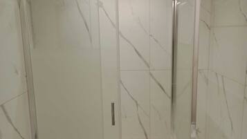 A bathroom with marble walls and a glass shower enclosure.
