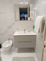 Un bagno moderno con un mobile lavabo bianco, un bidet, uno specchio e un porta asciugamani.