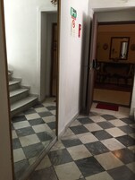 A hallway with checkered flooring, a staircase, and a door leading to a room with a red doormat.