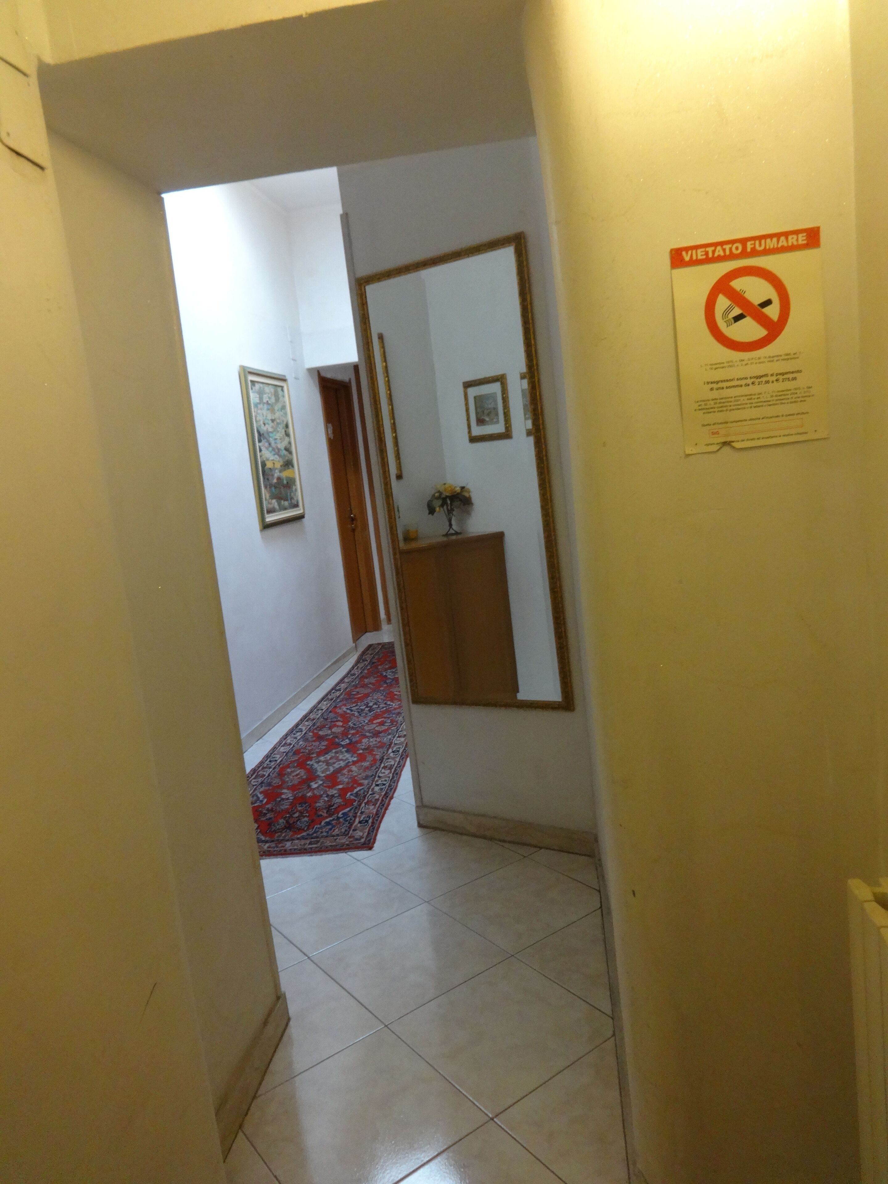 Un pasillo con suelo de baldosas, un tapete rojo estampado, una puerta de madera y un letrero en la pared.