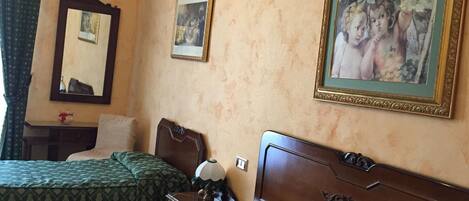 A hotel room with two beds, a wooden headboard, a nightstand, a lamp, and two framed pictures on the wall.