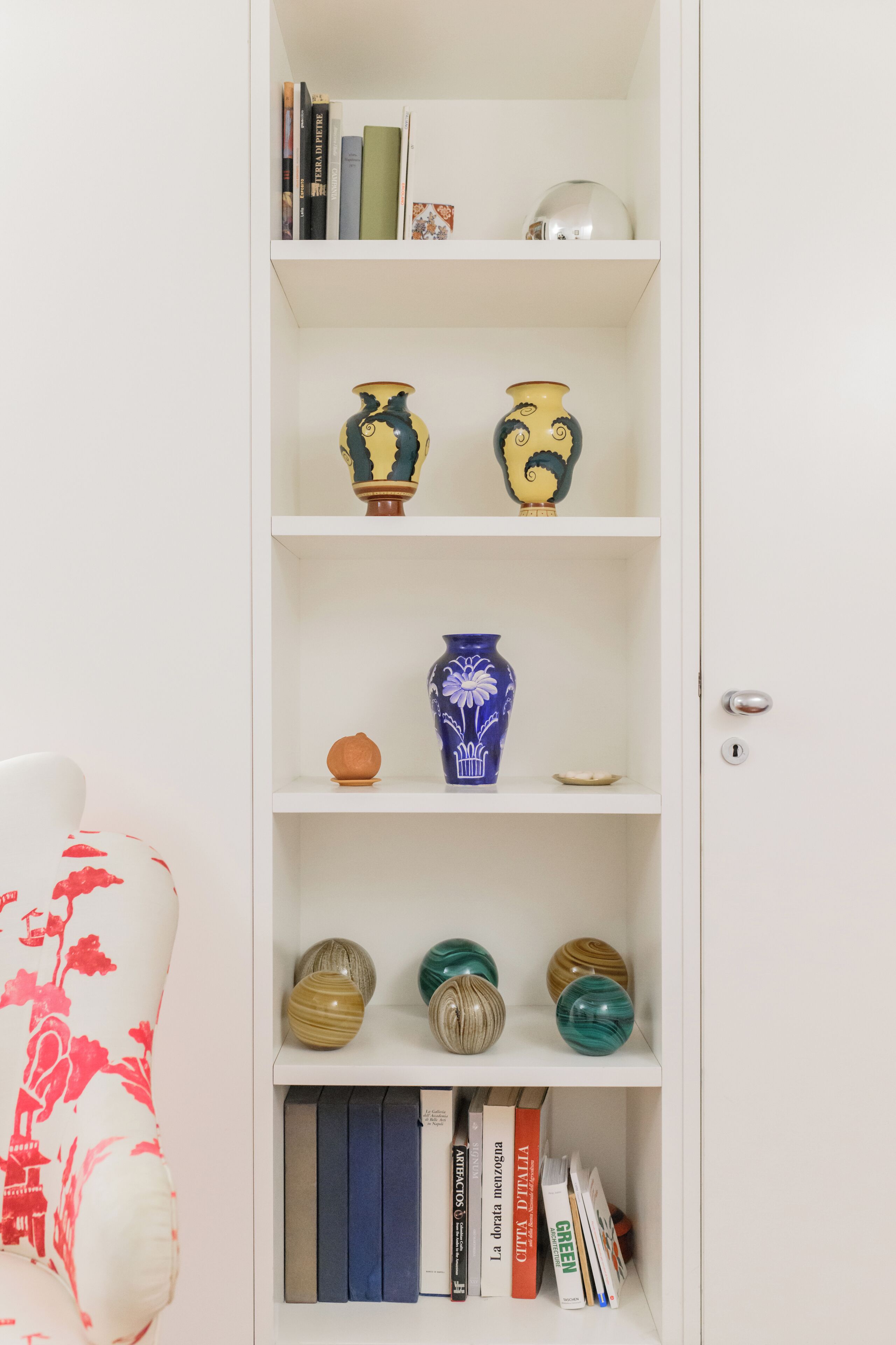 Una estantería blanca adornada con jarrones decorativos, libros y un pequeño globo terráqueo.