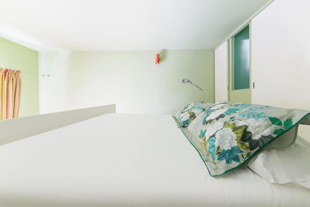 Un dormitorio con una cama grande, una mesita de noche, una lámpara y una ventana con cortinas.