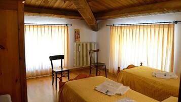 A room with two beds, wooden ceiling beams, a radiator, and curtains.