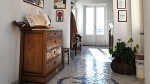 A hallway with a wooden dresser, a tiled floor with a decorative pattern, a door at the end, and a potted plant. - La Casa sul Mare (Procida)