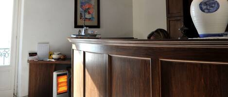 A wooden reception desk with a lamp, a framed picture on the wall, and a heater on the floor.